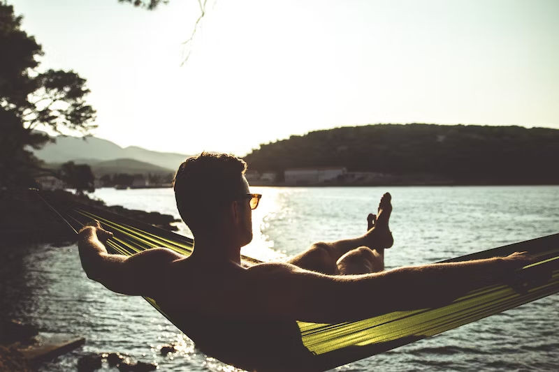 young man enjoying nature by the lake laying on the hamak